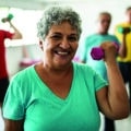 Portrait of senior woman lifting weights with classmates at the gym